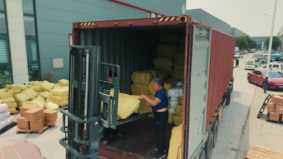 Workers loading forklift-stacked rolls of shade cloth into a shipping container at the factory yard